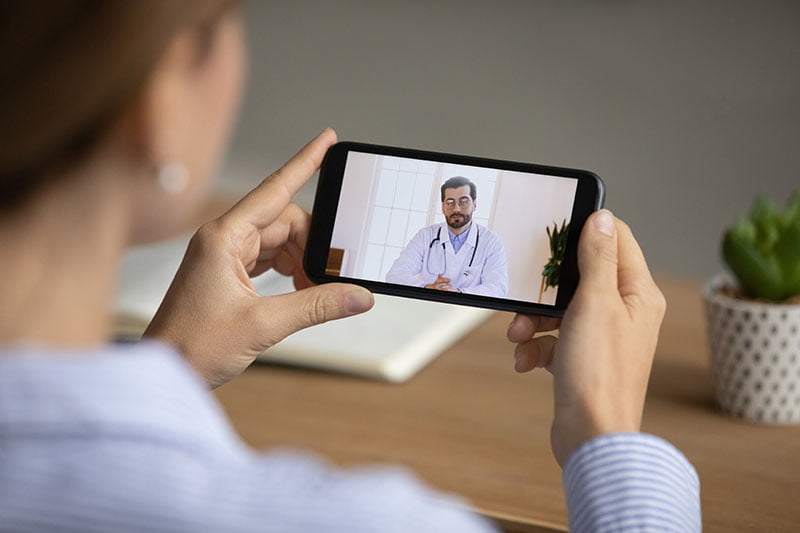 Close up back view of woman talk speak on video call on smartphone with male doctor or therapist. Female have online digital